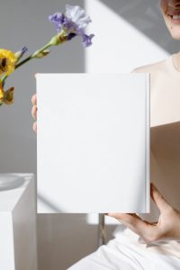 Minimalist blank book cover held in a bright room with flowers in the background.