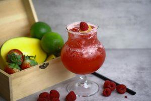 Chilled raspberry lemonade served with fresh fruits including mango, lime, and strawberries for a healthy refreshment.