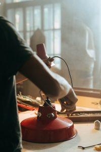 Person repairing red lamp in sunlit workshop, showcasing craftsmanship and tools.