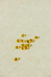 A collection of transparent golden capsules arranged on a neutral light background depicting supplements or vitamins.