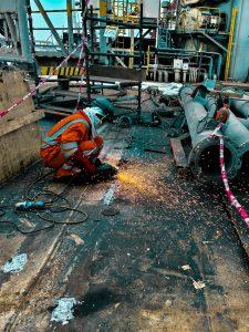 A worker in safety gear welds metal on an offshore rig, with sparks flying.