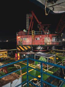 Nighttime view of an industrial offshore barge with cranes and equipment under artificial lighting.