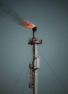A tall industrial flare stack releasing flame and smoke, set against a clear sky, captures the essence of industrial emissions.