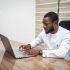 Stylish African man in a modern office using a laptop for business tasks.