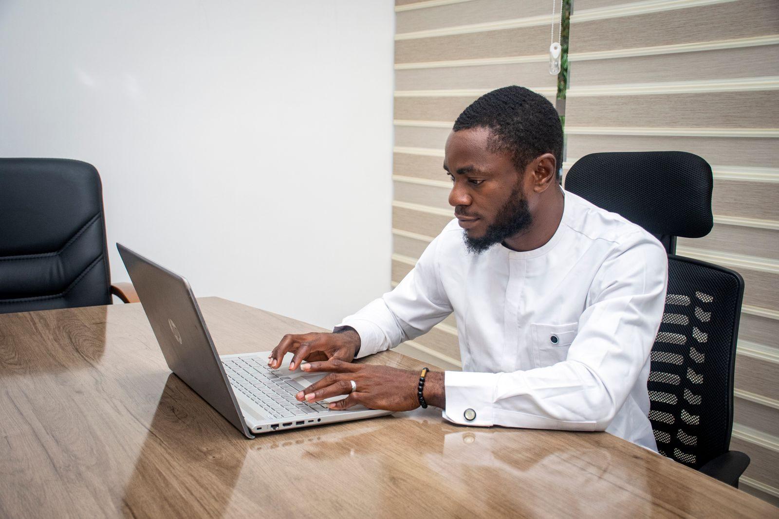 Stylish African man in a modern office using a laptop for business tasks.