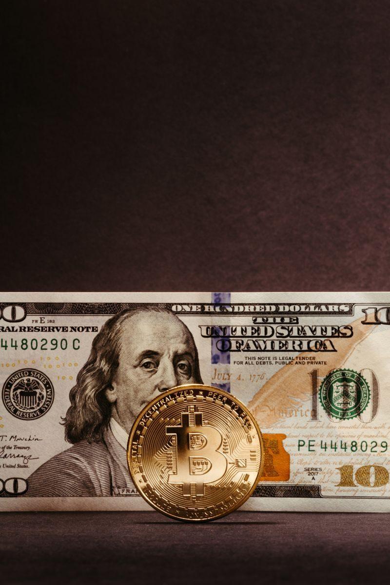 Golden Bitcoin coin against a US dollar bill, highlighting cryptocurrency's relation to traditional currency.