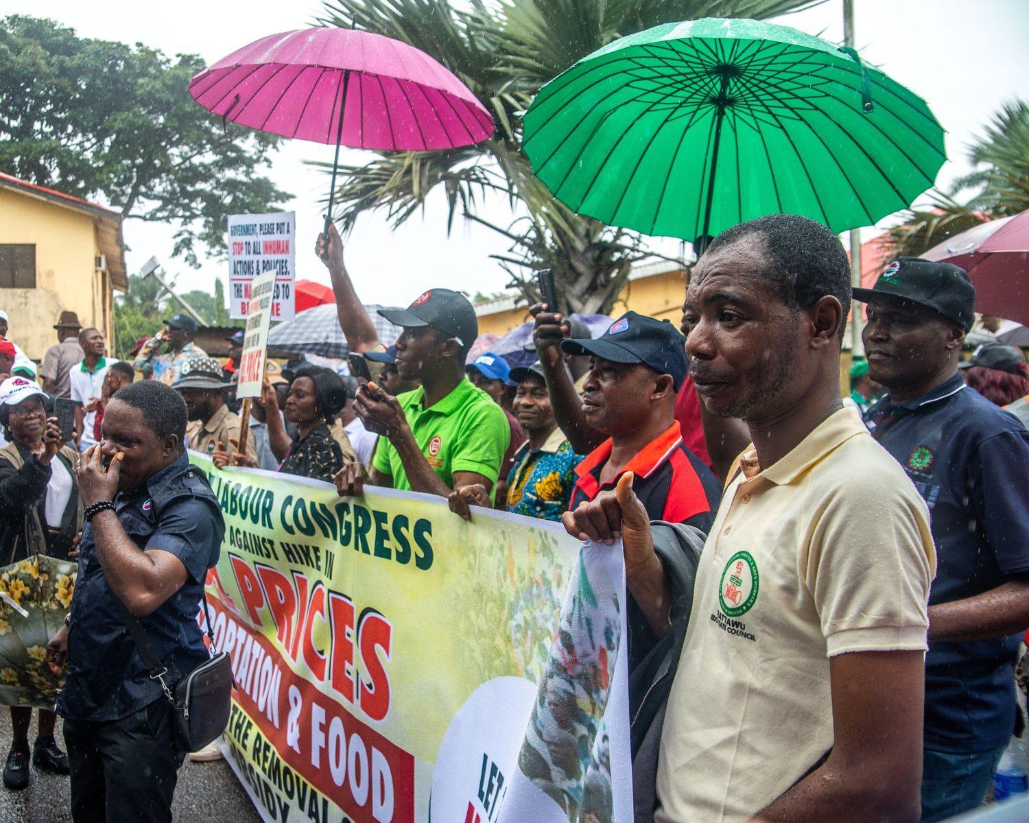 A diverse group of protesters with placards rally in the rain, advocating for economic change.