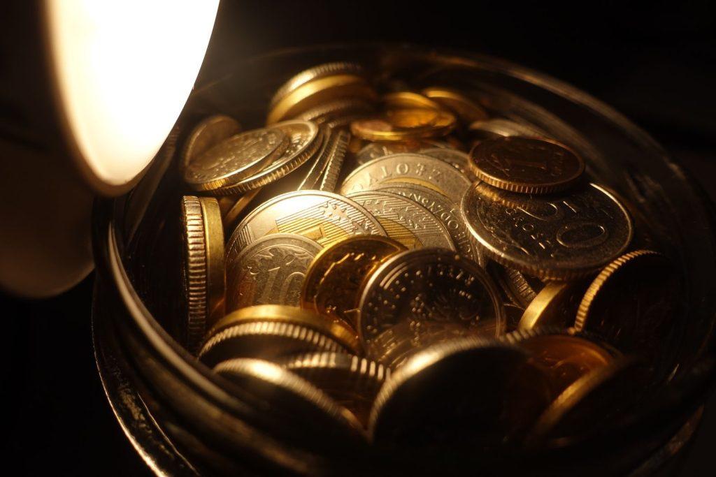 A detailed view of assorted coins in a jar under warm light, depicting financial wealth.
