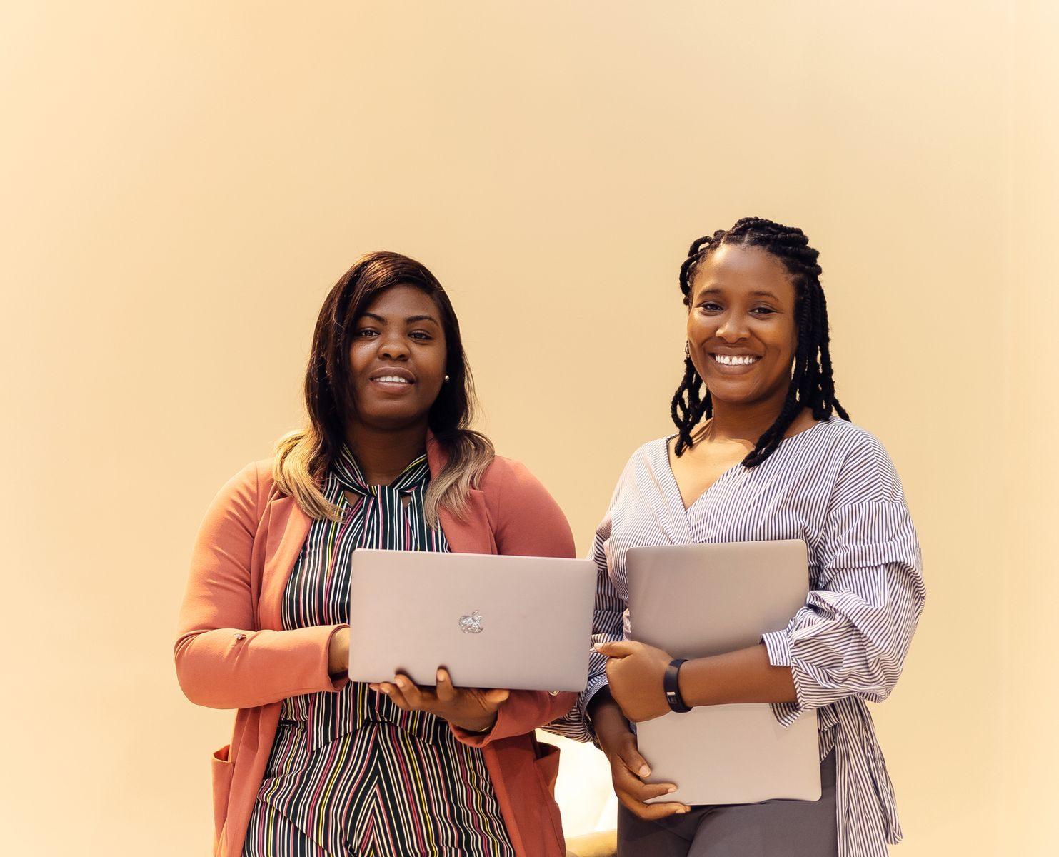 Professional African businesswomen smiling while working with laptops in a modern Lagos office setting.