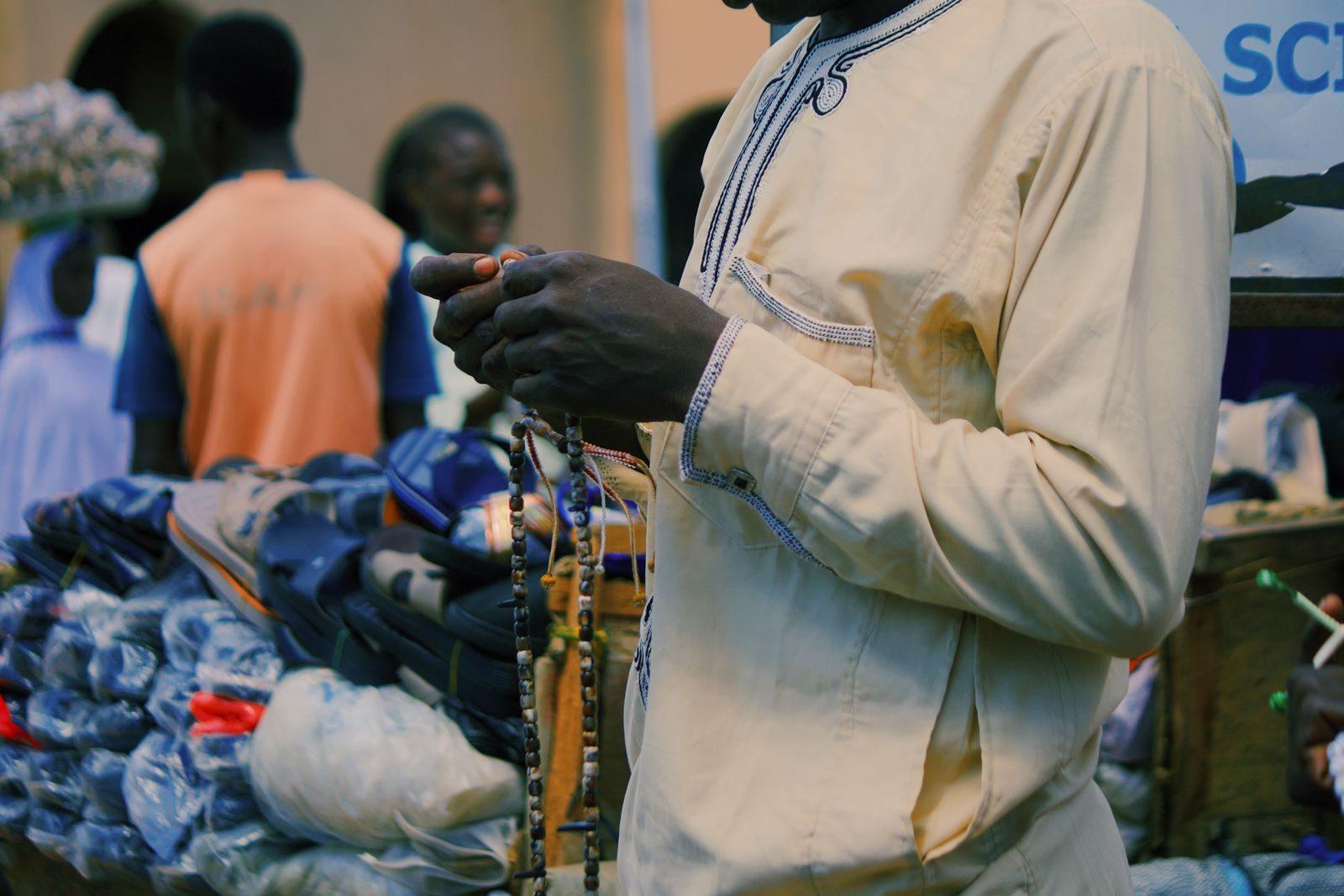 A man in traditional clothing sells beads at a vibrant outdoor market in Nigeria.