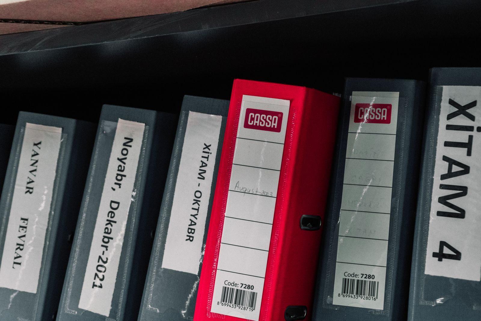 Color-coded office binders organized neatly in a storage shelf, featuring labels and a striking red binder.