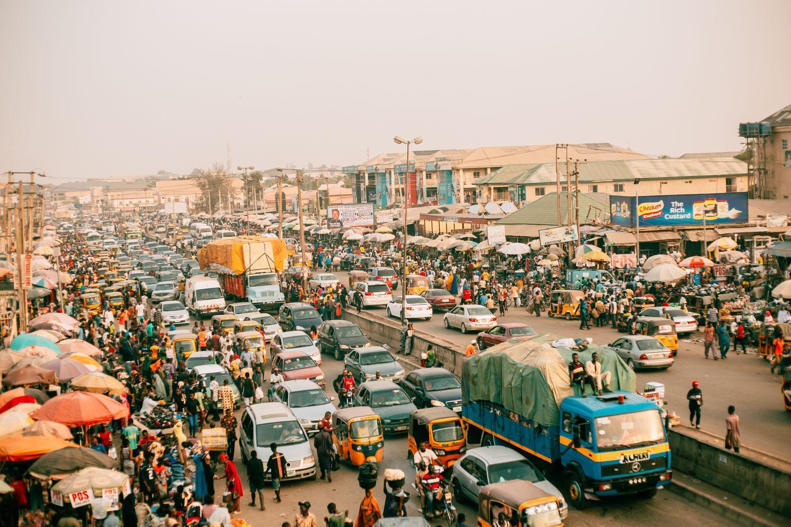 A busy street market scene with heavy traffic and numerous people in an urban setting.