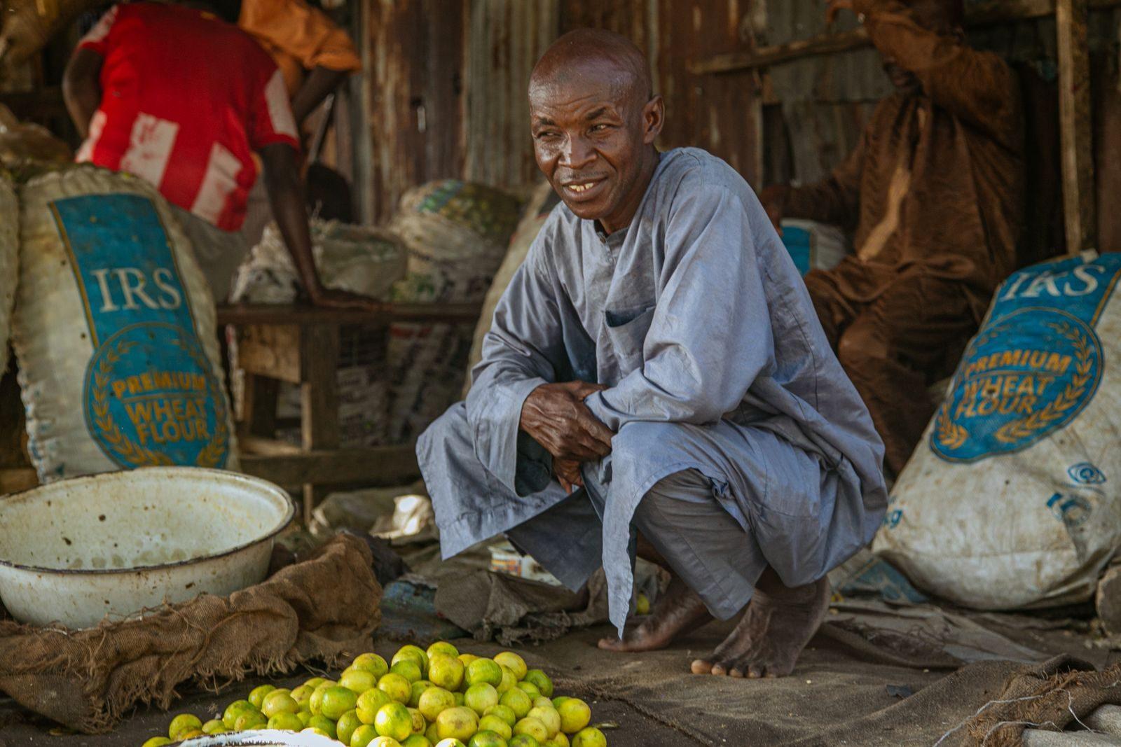 Portrait of a man squatting in a bustling African market in Maiduguri, Nigeria.