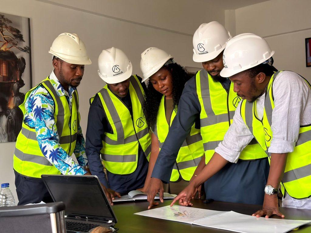 Photo by Harrun Muhammad A diverse team of five engineers in safety gear examines construction plans indoors.