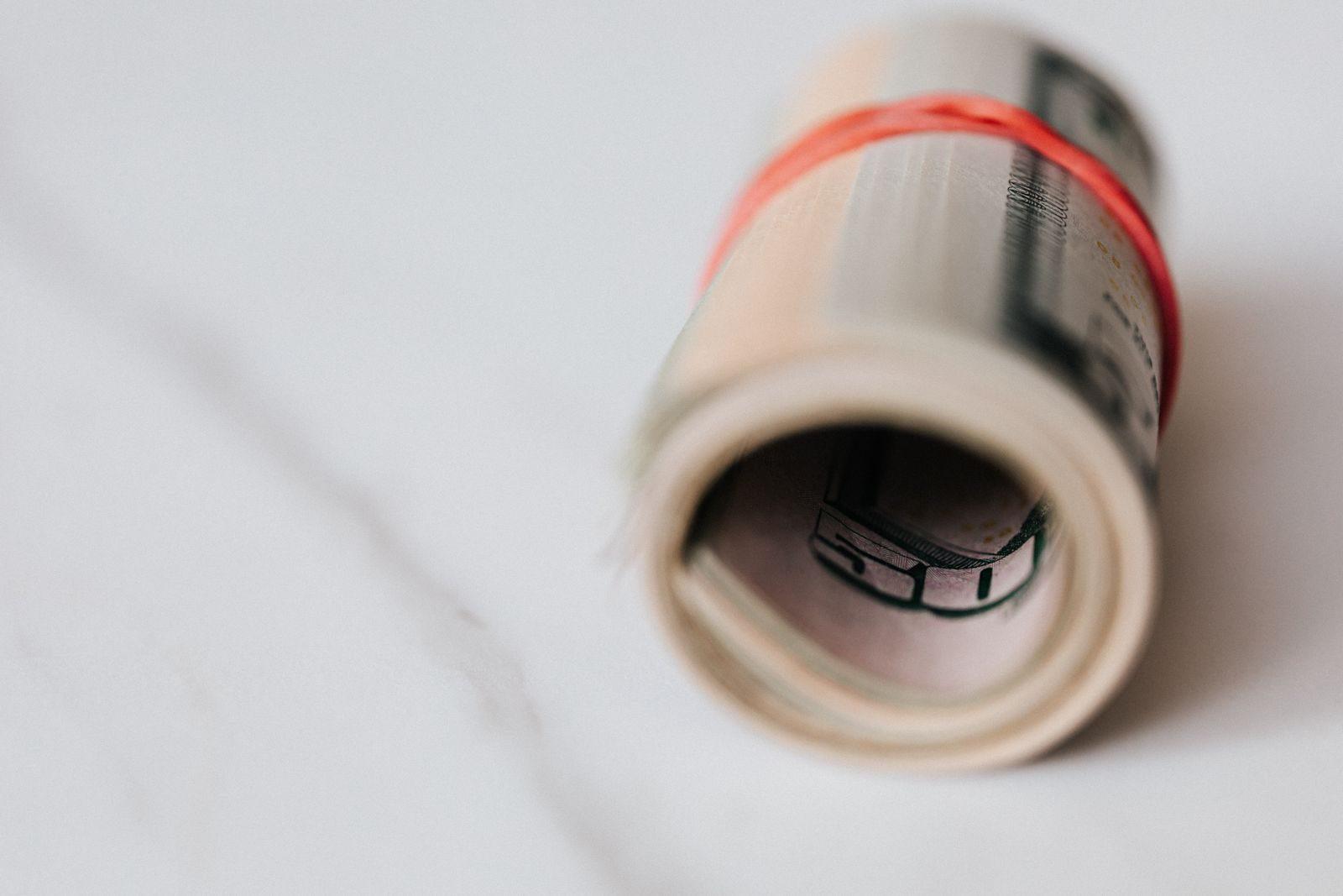 Pack of fifty dollar bills twisted into roll and tightened with red rubber band on white background