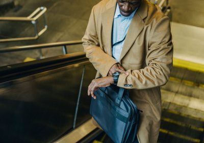 From above crop punctual African American businessman riding escalator and checking time on wristwatch while leaving metro station