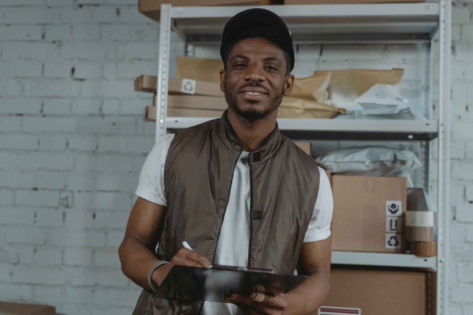 Warehouse employee holding a clipboard, surrounded by packages and smiling.