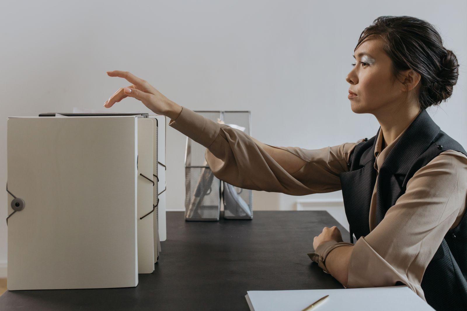 Asian woman efficiently organizing documents at an office desk.
