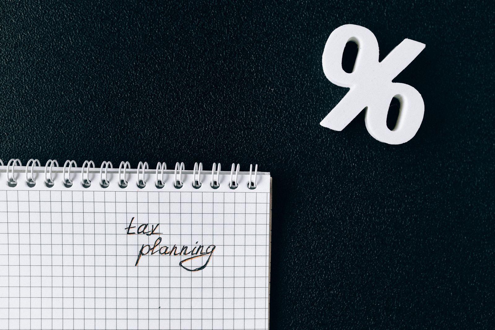 A notebook with 'tax planning' written on a grid paper next to a percent symbol on a black background.