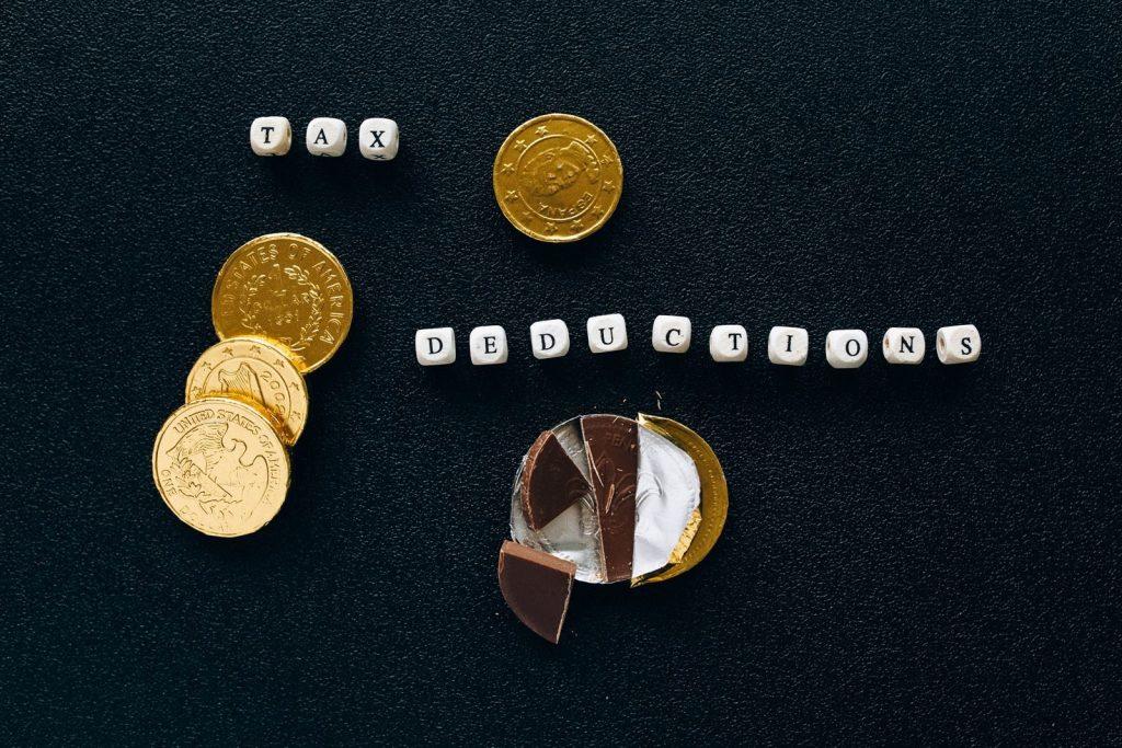 Creative concept of tax deductions using chocolate coins and letter tiles on a black background.