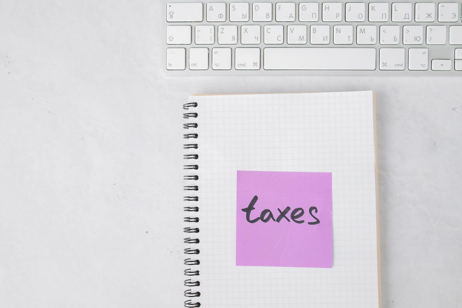 Top view of a notebook with a 'taxes' sticky note beside a keyboard, ideal for finance themes.