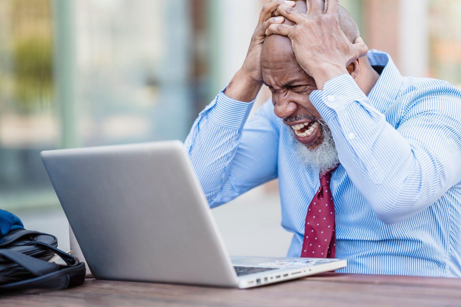 African American man showing frustration with laptop outdoors.