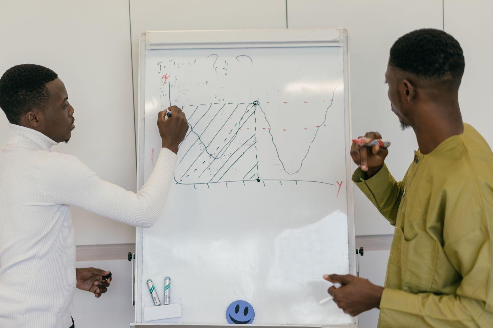 Two businessmen analyzing data on a whiteboard in an office setting.