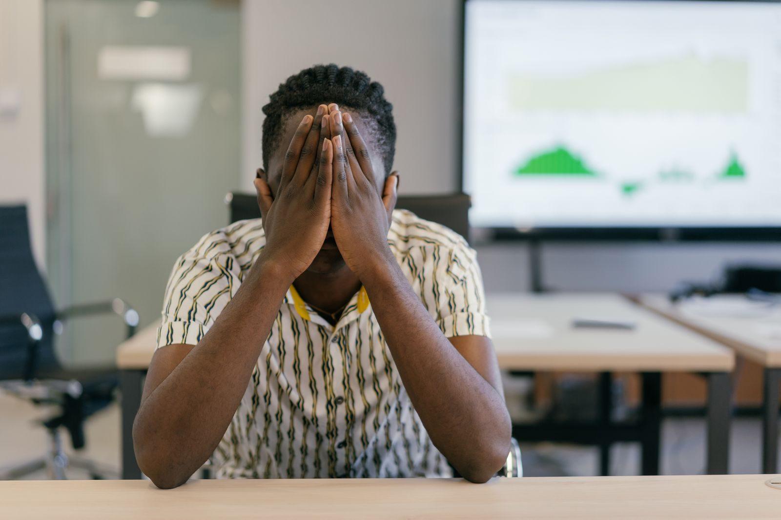 A stressed employee covering face in a modern office, depicting work pressure.