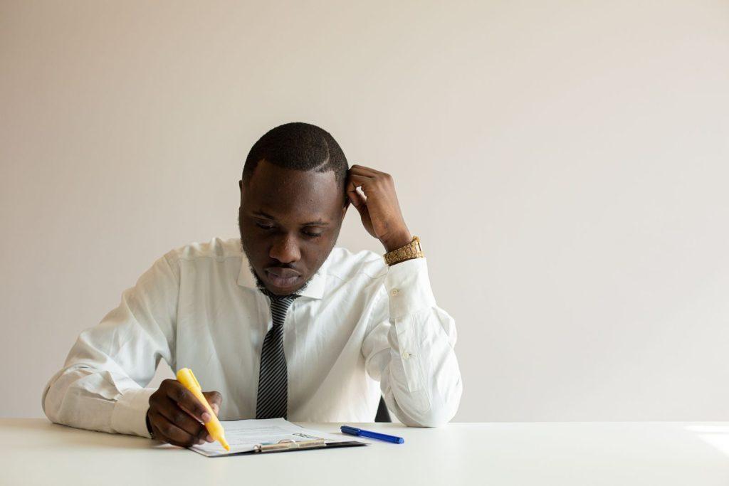 Photo by Monstera Production Businessman in white shirt taking notes at desk with pencil, deeply focused on work.