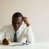 Businessman in white shirt taking notes at desk with pencil, deeply focused on work.