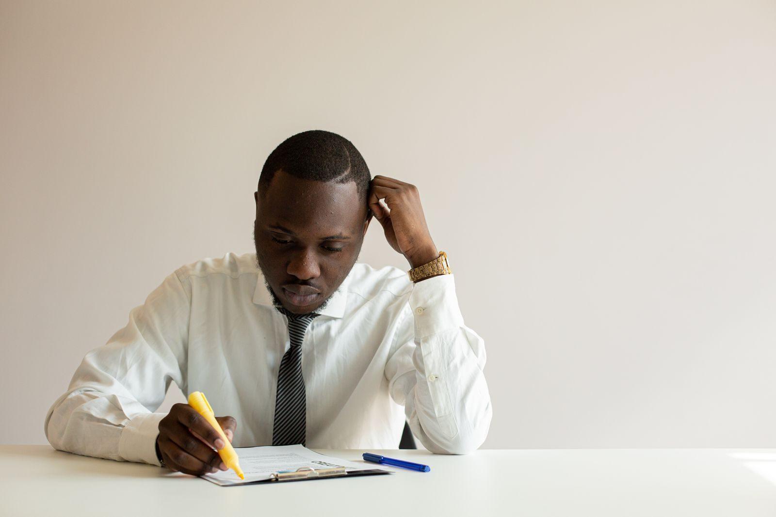 Businessman in white shirt taking notes at desk with pencil, deeply focused on work.