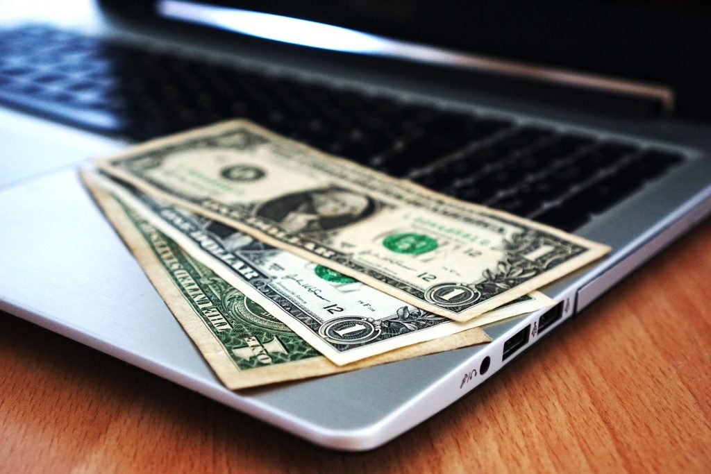 Photo by Pixabay Close-up of US dollar bills placed on a laptop symbolizing digital finance and economy.