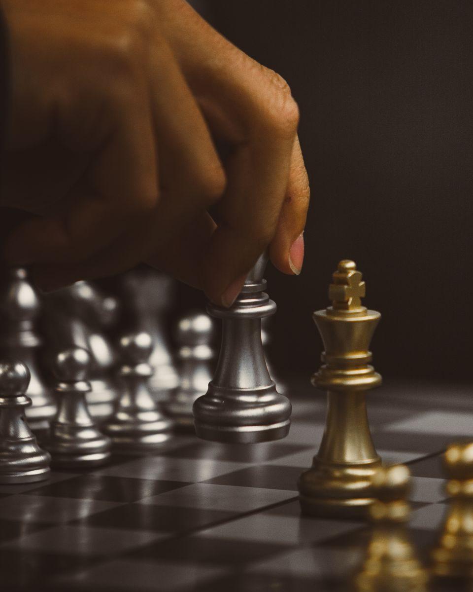 Close-up of a chess player making a move with metallic chess pieces, emphasizing strategy and focus.