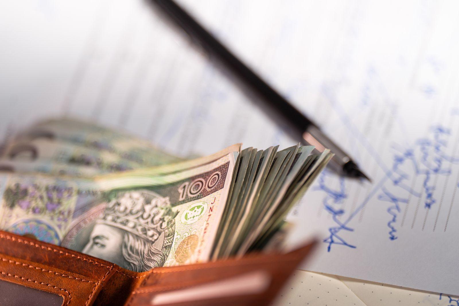Stack of Polish zloty banknotes with pen and document, financial concept.