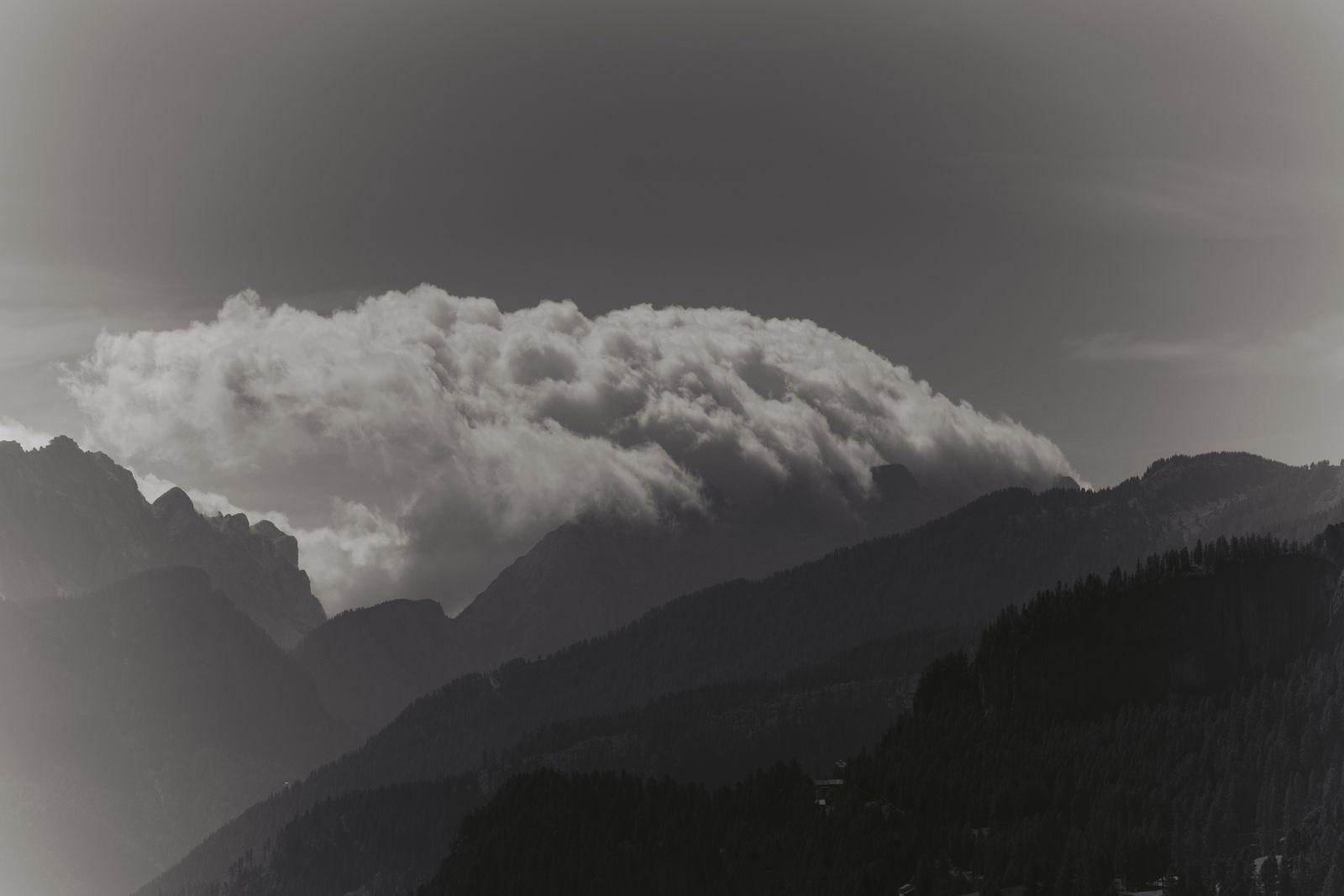 A dramatic mountain scene with dense clouds forming over rugged terrain, captured in monochrome.