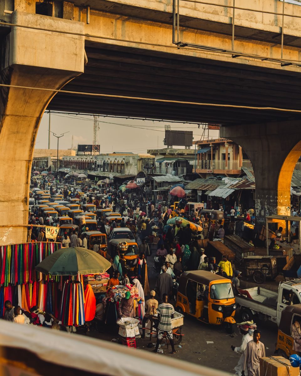 Bustling Kano market scene under an overpass, showcasing a lively atmosphere and colorful local commerce.