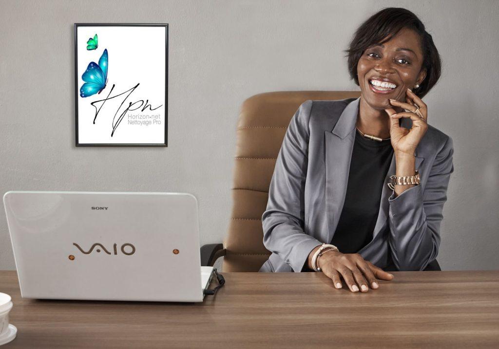 Smiling African American businesswoman in a gray blazer sitting at a desk in an office setting.