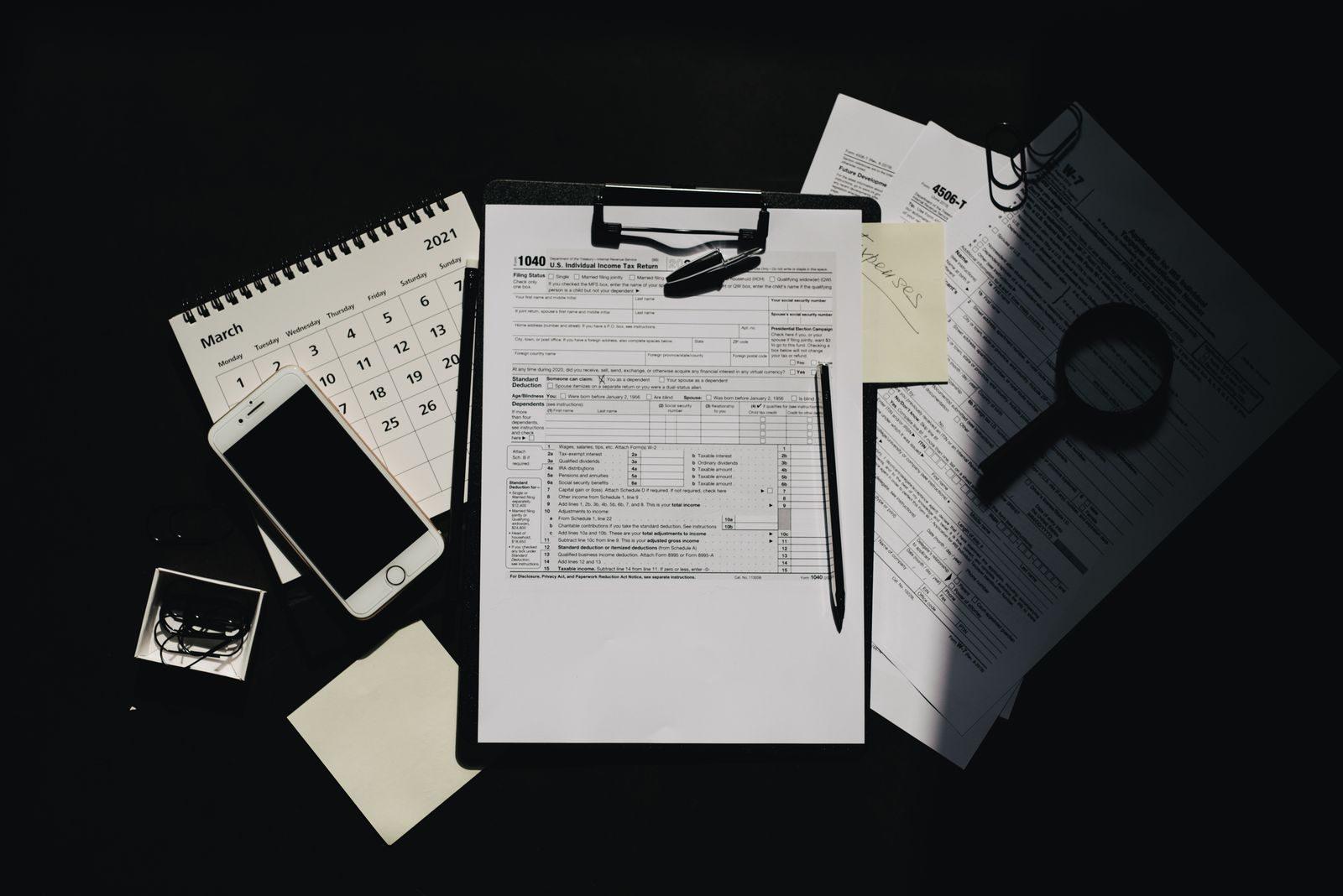 Flat lay of tax documents, calendar, and smartphone on a dark surface, symbolizing tax preparation.
