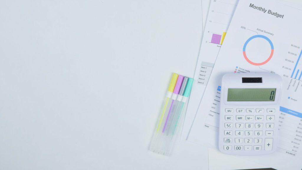 Minimalist office desk with a calculator, budget planning documents, and colorful pens.