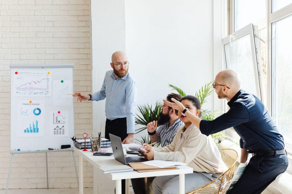 Photo by https://kaboompics.com/ A group of professionals engaged in a business meeting, discussing financial graphs on a whiteboard.