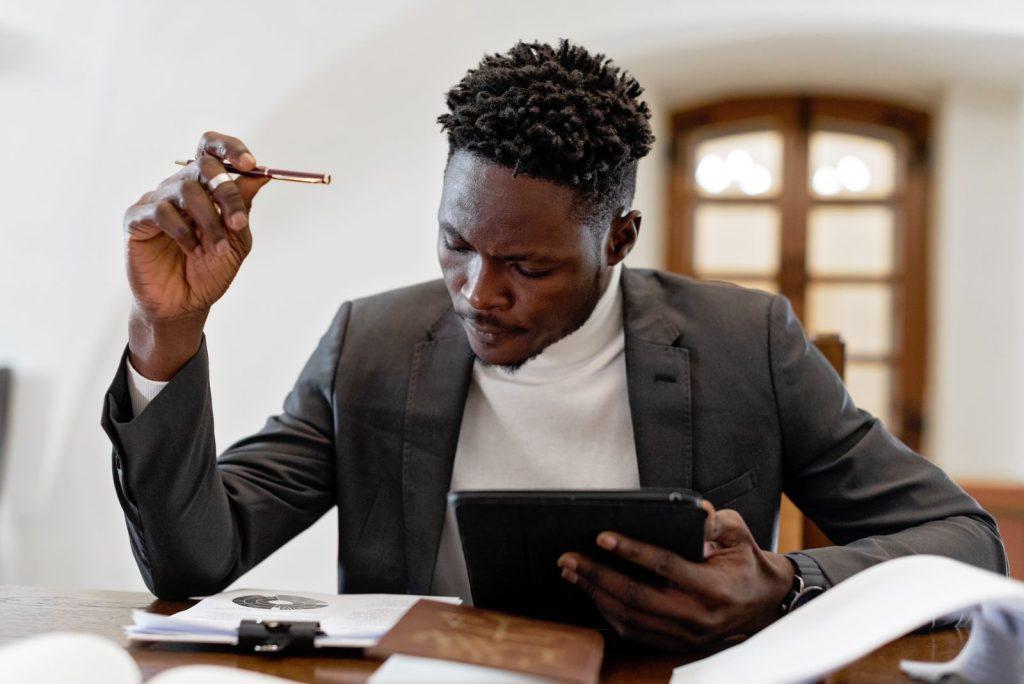 Photo by Mikhail Nilov Confident businessman working on a tablet with documents in an office setting.