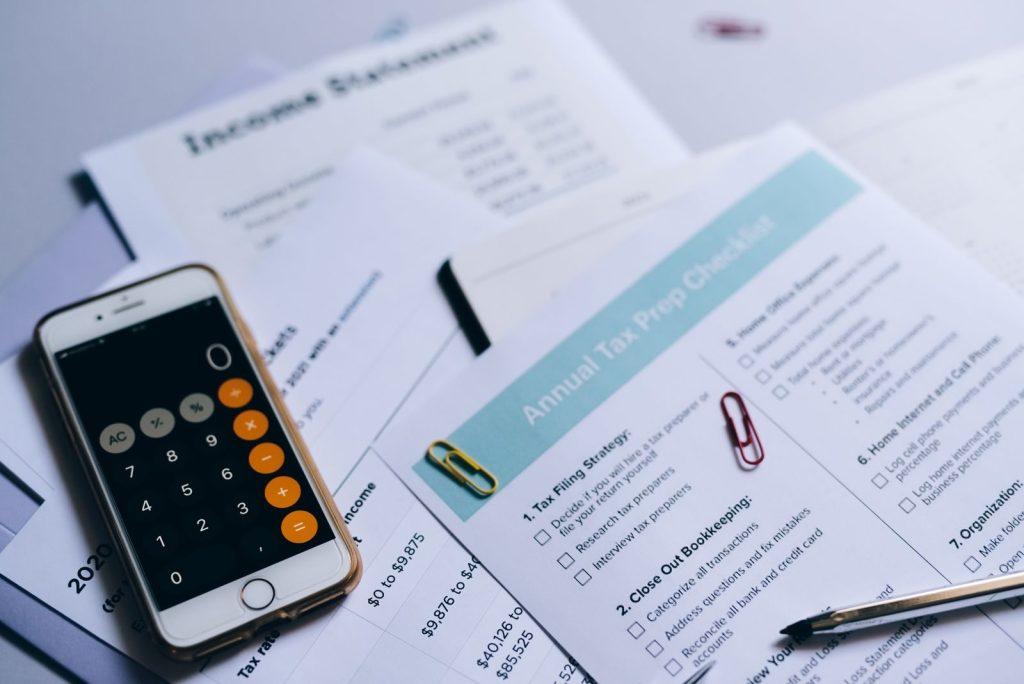 Photo by Leeloo The First Tax preparation setup with documents, smartphone calculator, and checklist.