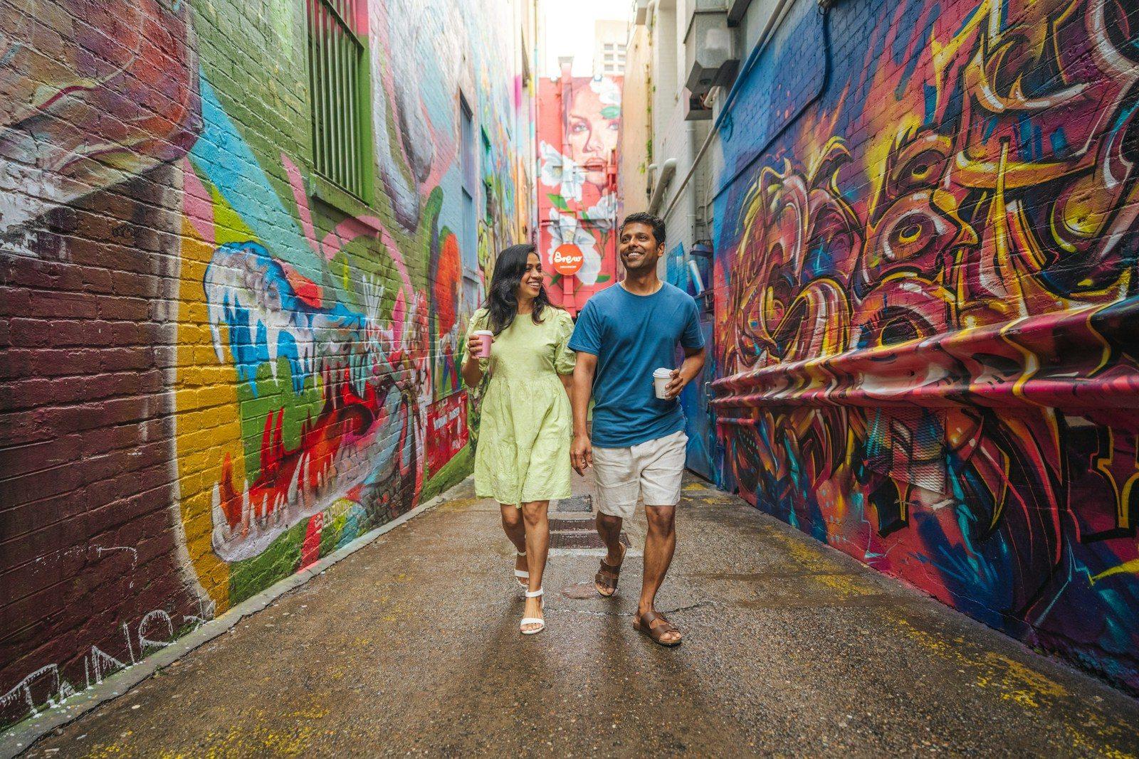 A woman and a man walking through a narrow alleyway with colorful graffiti walls