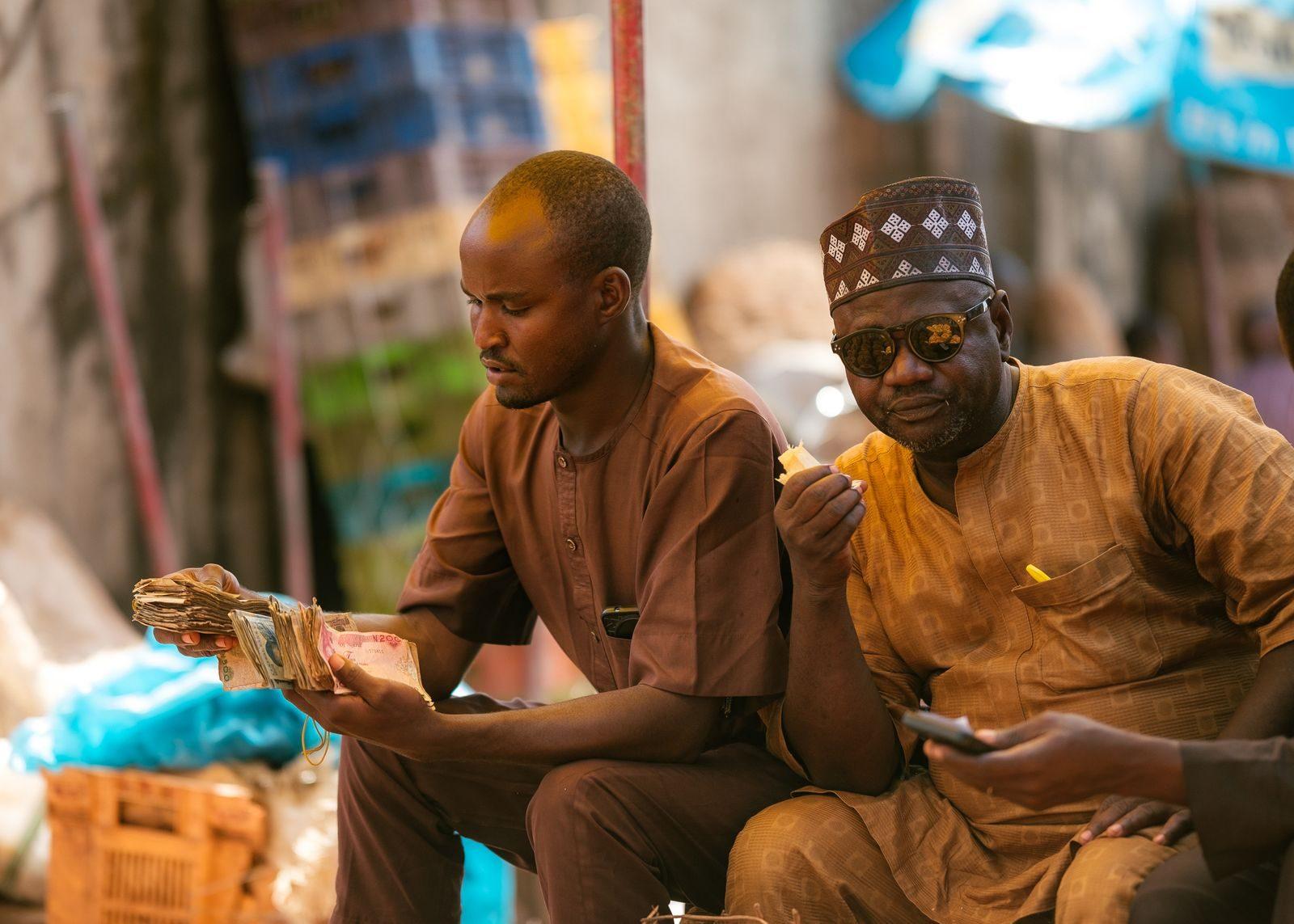 Men interacting and counted money at a market in Tudun Wada, Nigeria.