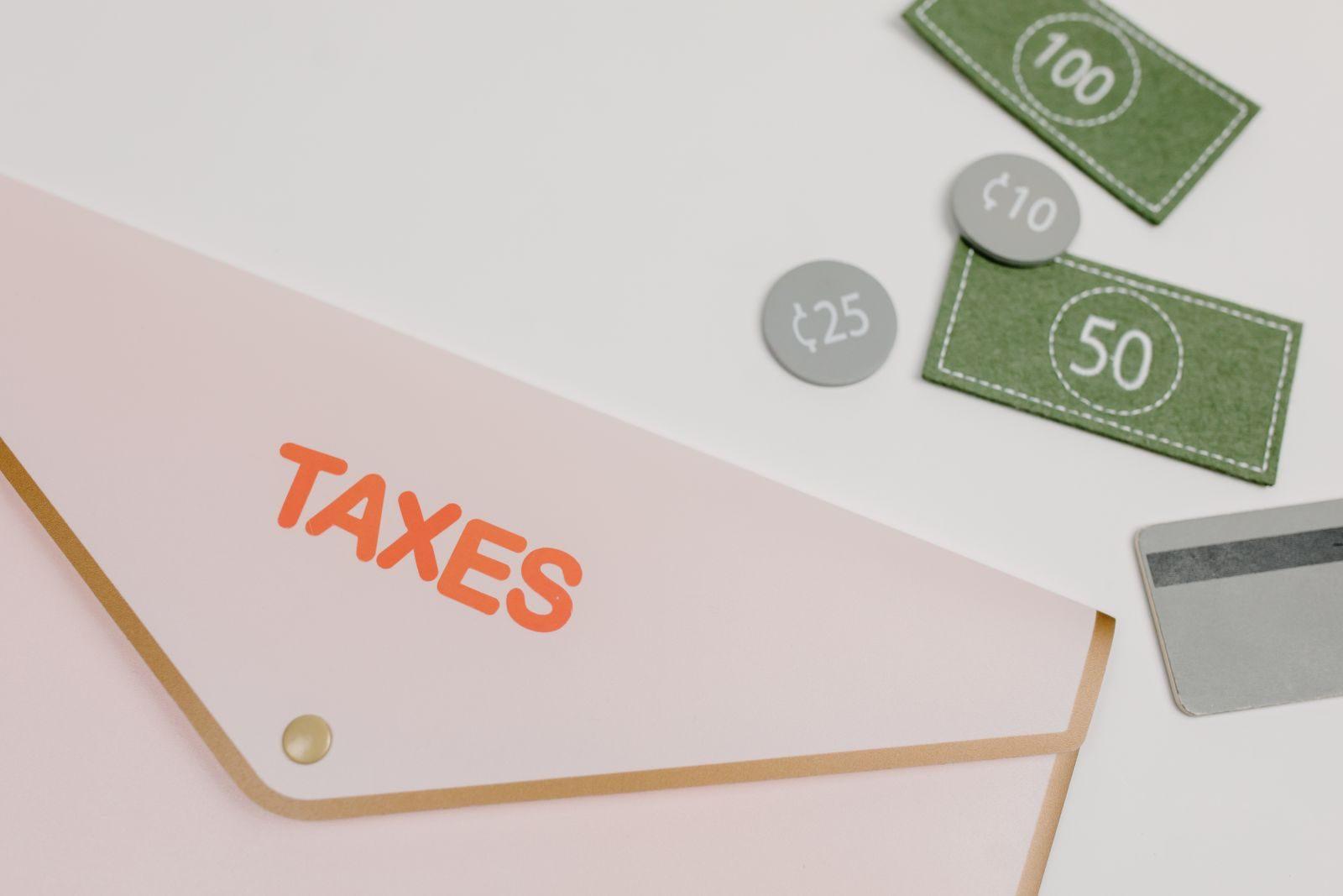 Pink envelope labeled 'TAXES' with play money and card on white background.
