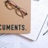 Flat lay of office supplies including documents, calendar, and eyeglasses on a desk.